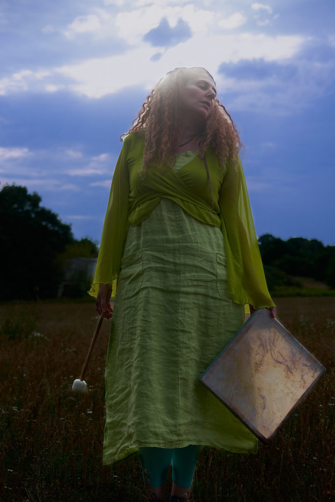 Raphaela Gilla on a summer meadow holding her shaman square drumm